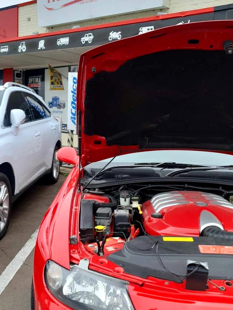 A car with the bonnet up having its battery replaced